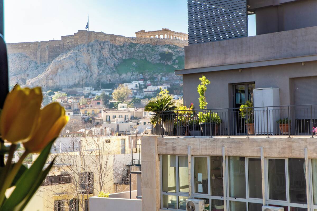 A building with a balcony, a view of a historic fort, and a flower in the foreground.