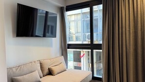 Una sala de estar moderna con un sofá, un televisor de pantalla plana en la pared y un amplio ventanal con cortinas.