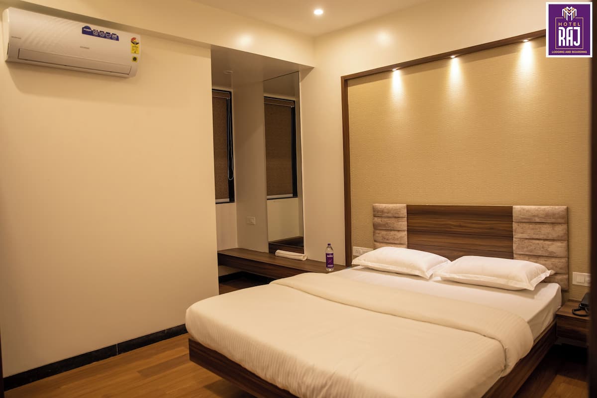 A hotel room with a bed, a mirror, a wall-mounted air conditioner, and a wooden headboard.