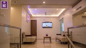 Un espace d’accueil d’hôtel comprenant un comptoir de réception, un téléviseur fixé au mur et un coin salon avec des canapés.