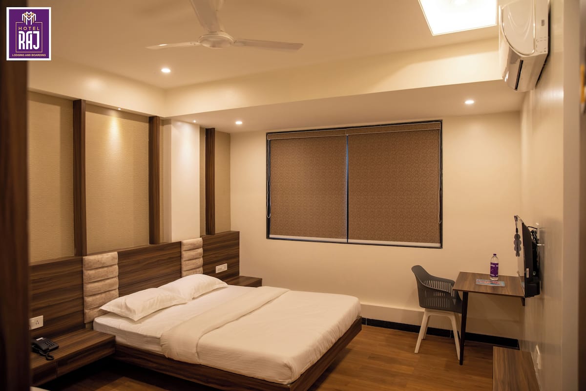 A hotel room with a bed, bedside table, desk, chair, and a window.