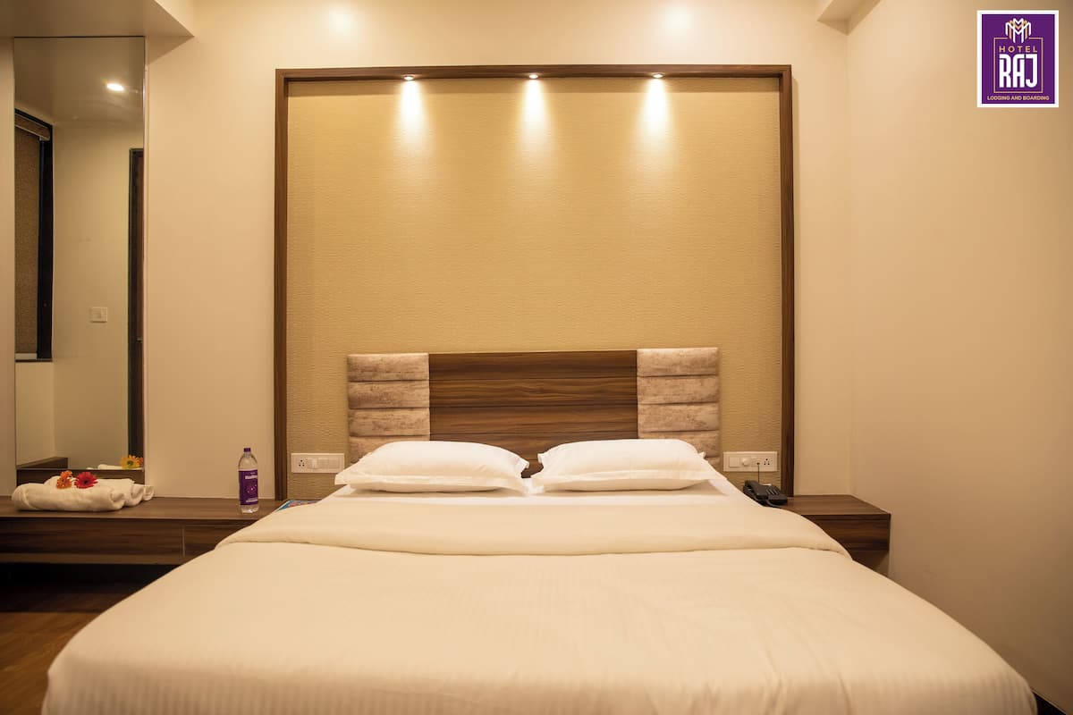 A modern hotel room with a large bed, a wooden headboard, and a nightstand with a phone and a bottle.