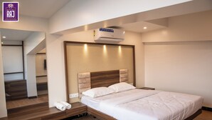 Une chambre d’hôtel moderne avec un lit en bois, un banc intégré avec des serviettes, un climatiseur mural et un miroir qui reflète la pièce.