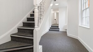 A staircase with a white railing and dark carpeted steps leading to an upper floor. - WhiskAwayStays - No. 58 Studio - No. 3 (Worcester)