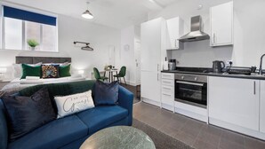 A modern apartment with a blue sofa, a dining area, a kitchenette, and a bed with green and white bedding. - WhiskAwayStays - No. 58 Studio - No. 3 (Worcester)