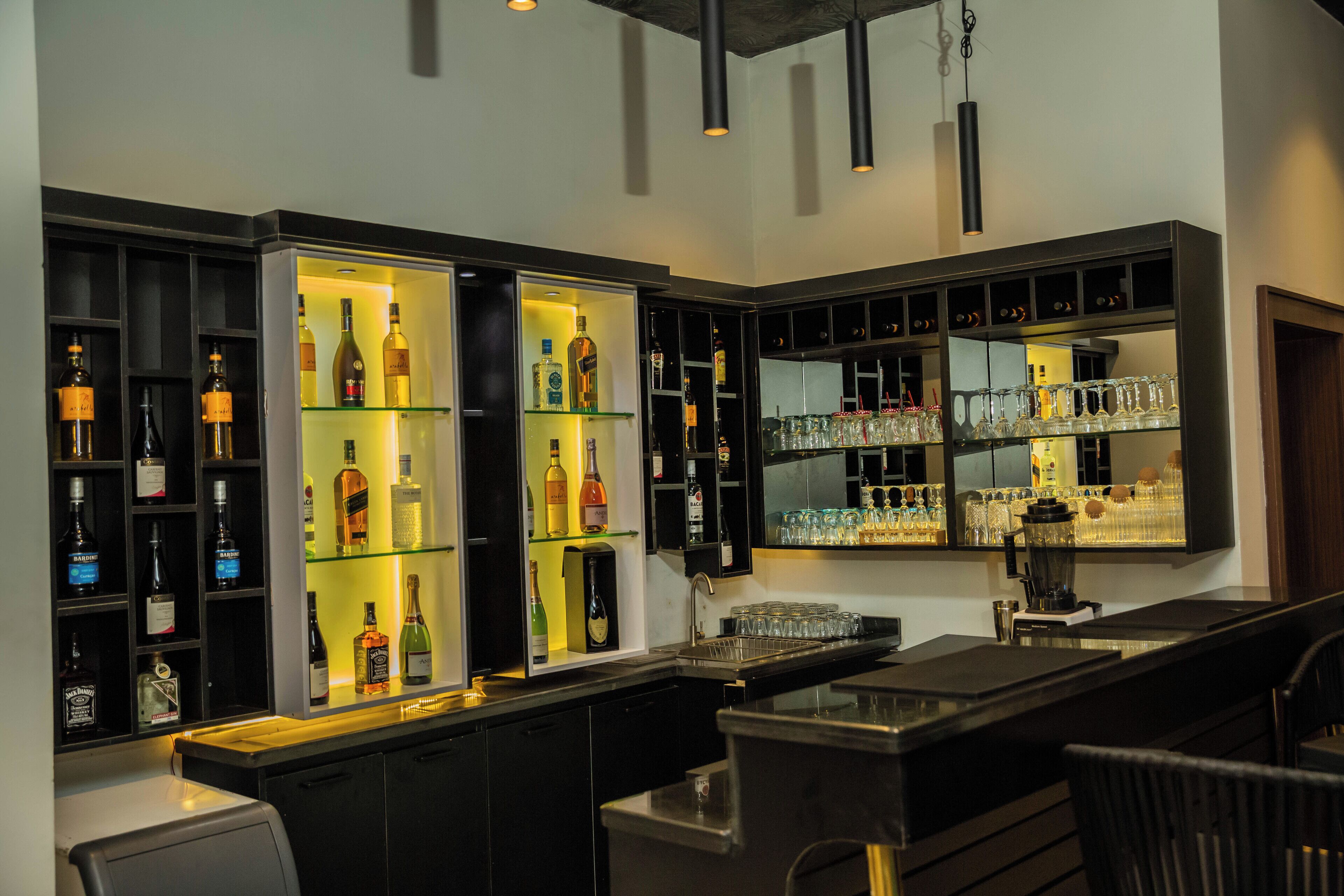 A bar area with shelves of liquor bottles, glasses, and a blender.