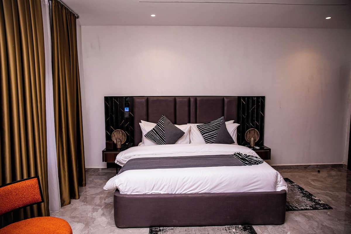 A modern bedroom with a large bed, dark headboard, and two bedside tables with lamps.