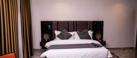 A modern bedroom with a large bed, dark headboard, and two bedside tables with lamps.