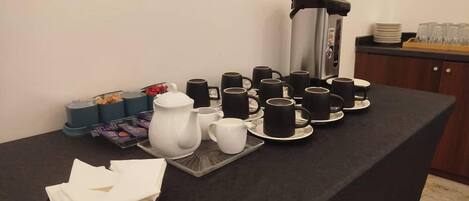 A table set with black cups, saucers, a white teapot, and a coffee maker.