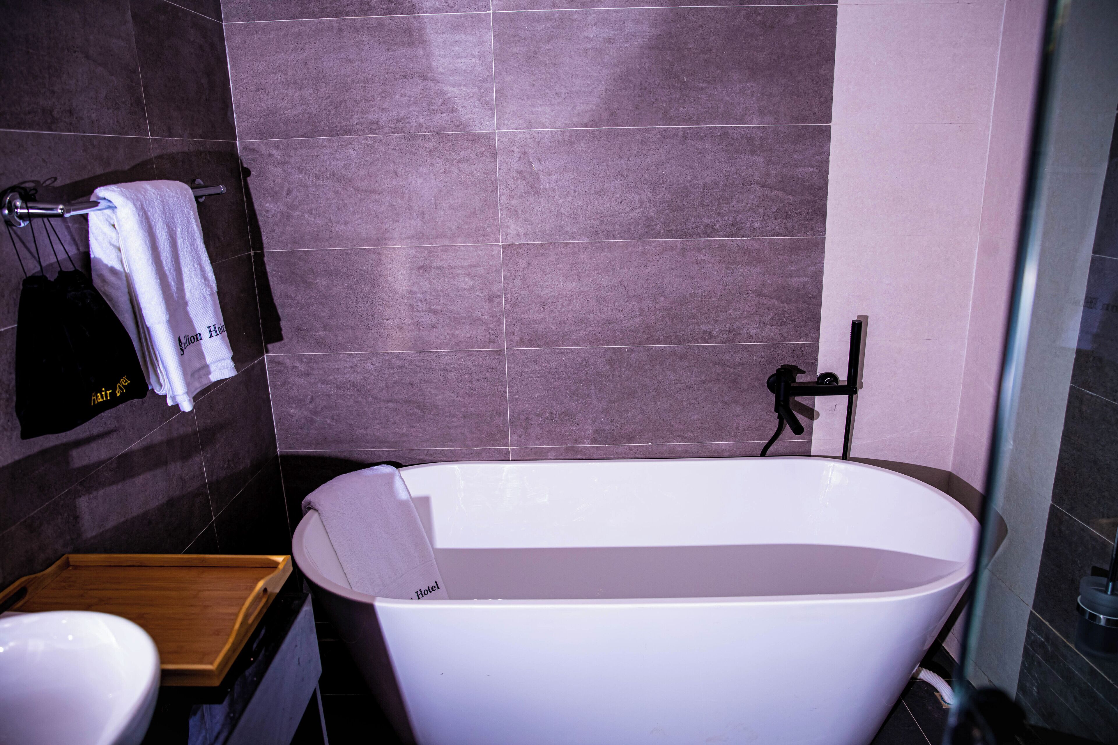 A modern bathroom with a freestanding bathtub, a wooden tray, and a towel rack with towels.