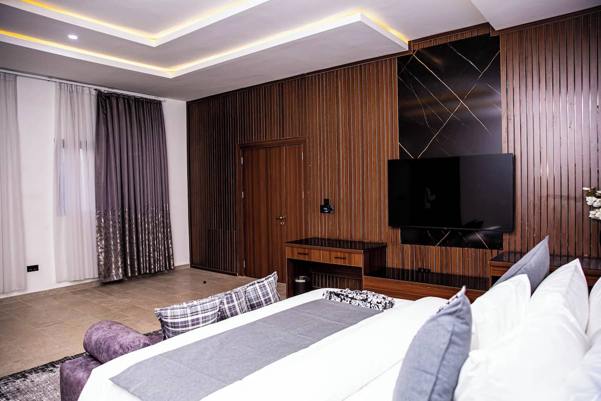 A modern bedroom with a large bed, a desk, and a TV mounted on a wooden wall.