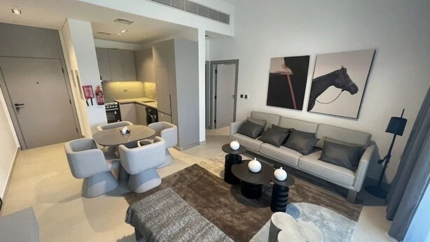 A modern living room with a sofa, coffee table, and seating area. There is a kitchen in the background.