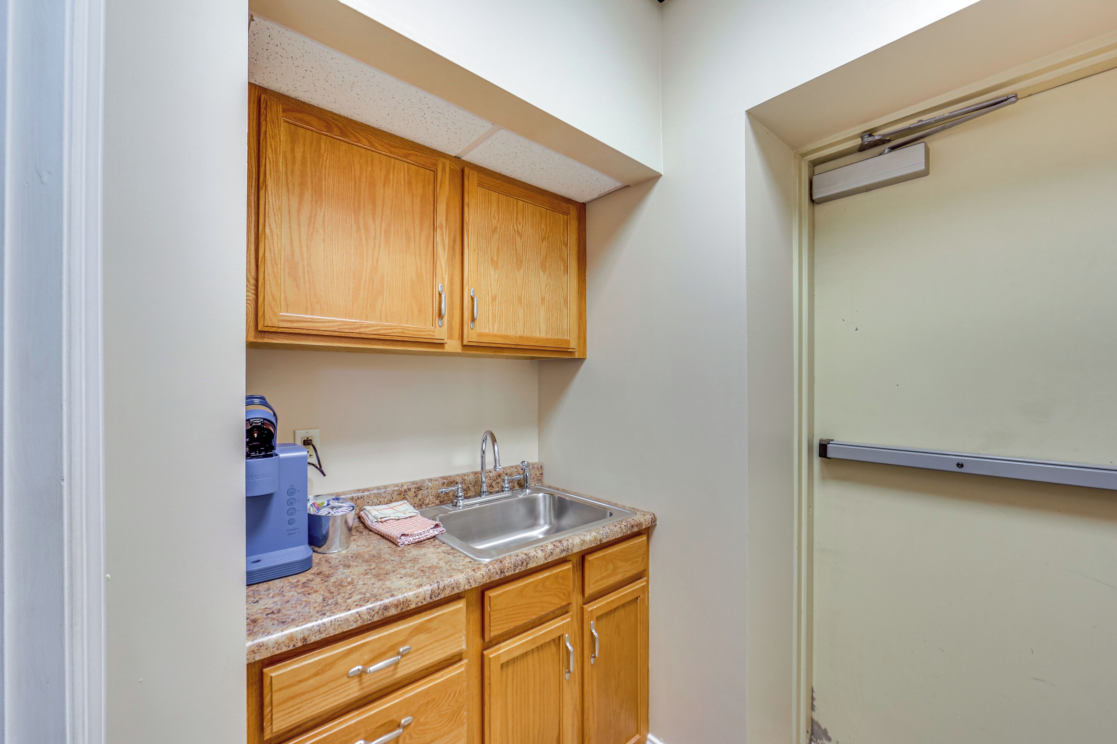 A kitchen with wooden cabinets, a stainless steel sink, and a coffee maker.