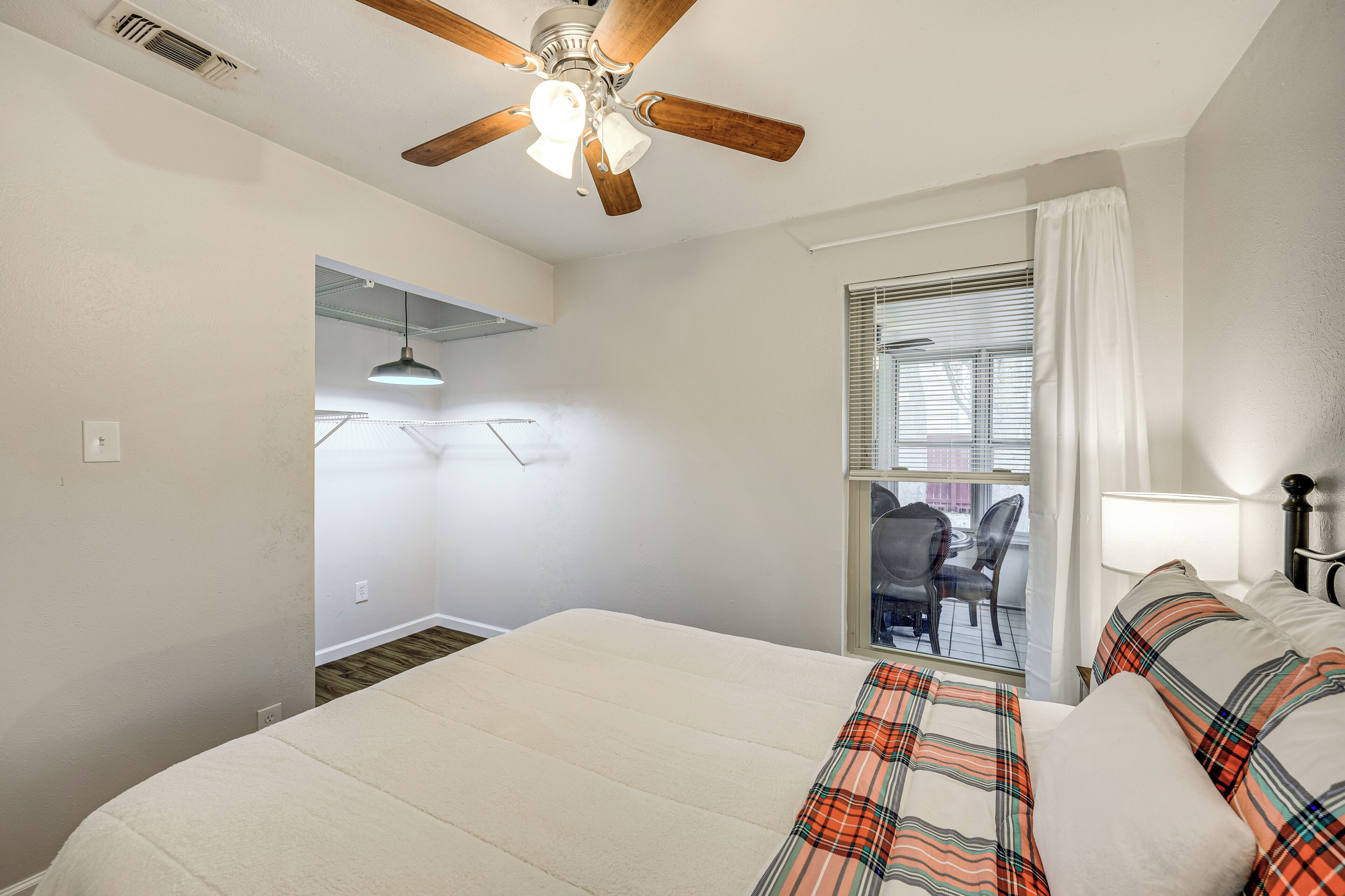 A bedroom with a bed, a ceiling fan, a window with curtains, and a view of the outside.