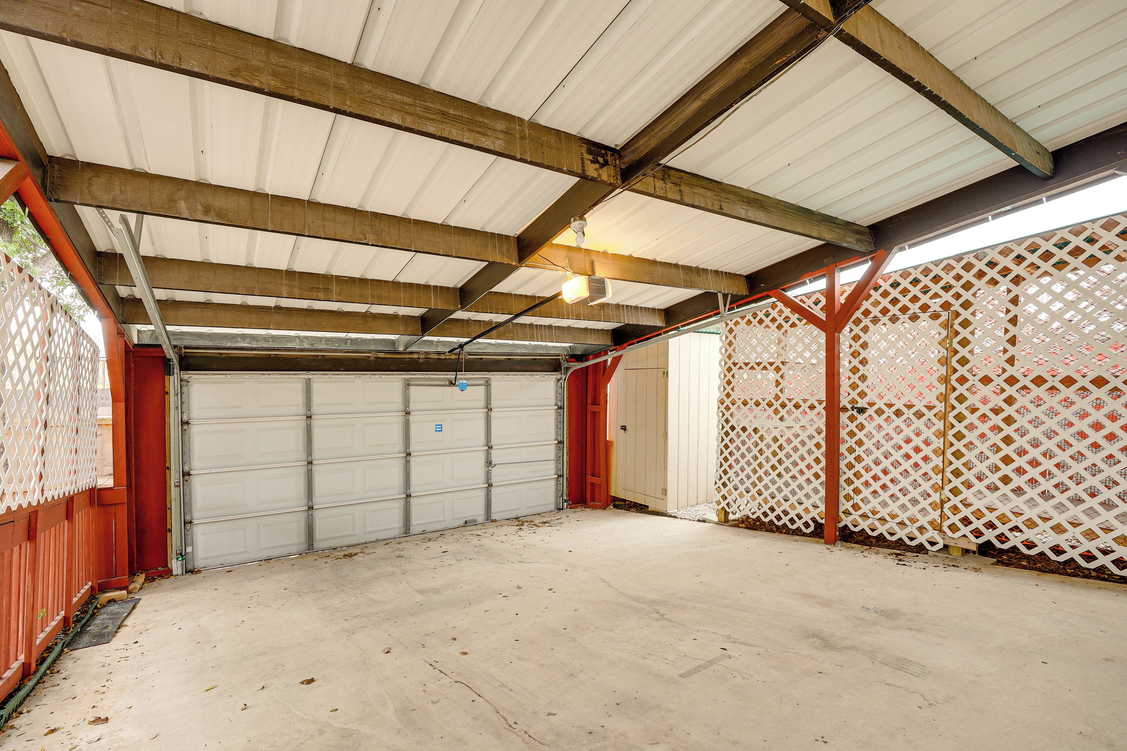 Un espace de stationnement couvert, doté d’une porte de garage, de poutres en bois et d’une clôture à treillis.