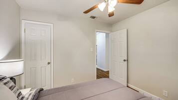 A bedroom with a bed, a ceiling fan, and a door leading to another room.