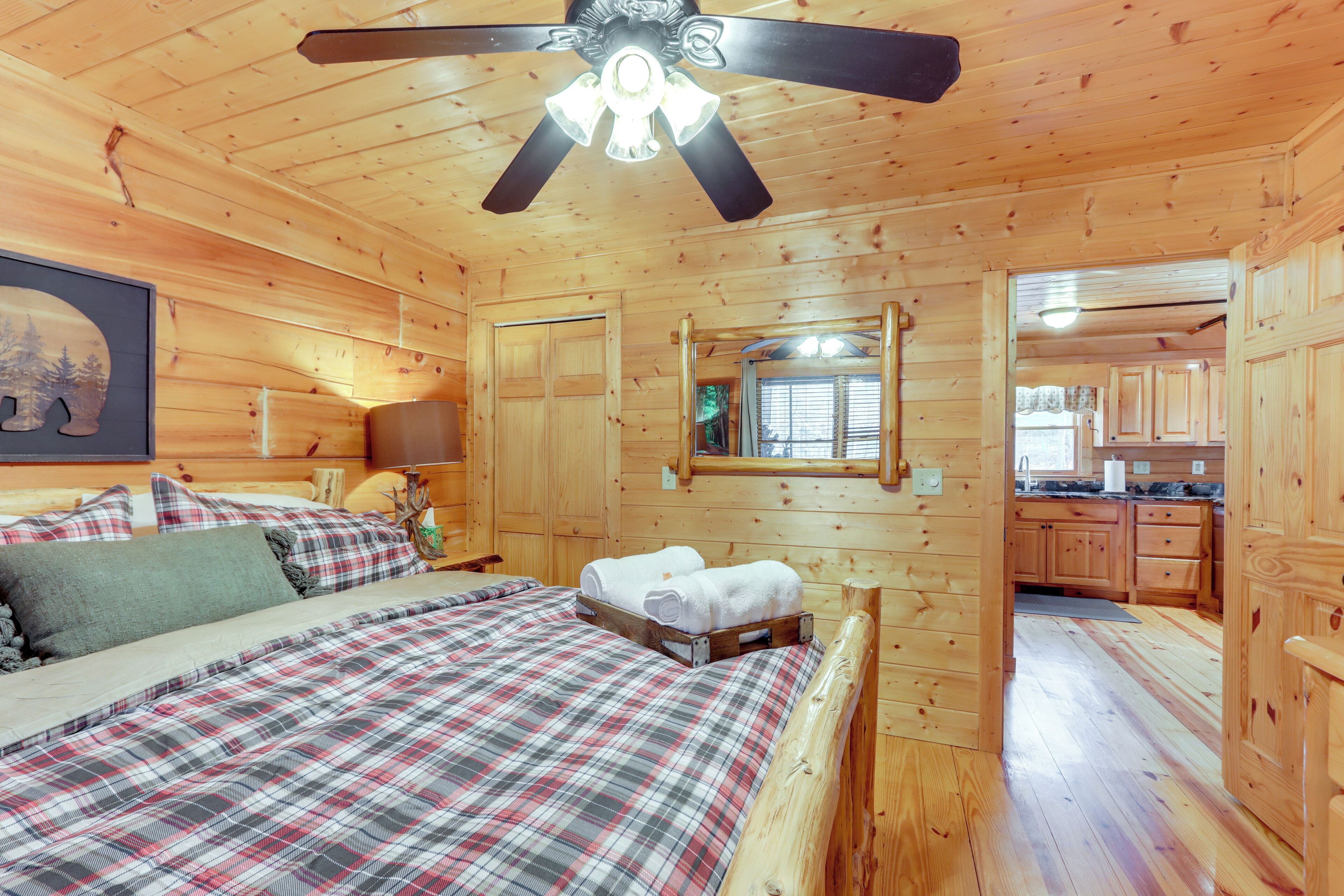 Une chambre dans une cabane en bois, avec un lit, un ventilateur de plafond et une vue sur la cuisine.