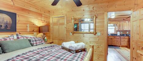 Une chambre dans une cabane en bois, avec un lit, un ventilateur de plafond et une vue sur la cuisine.