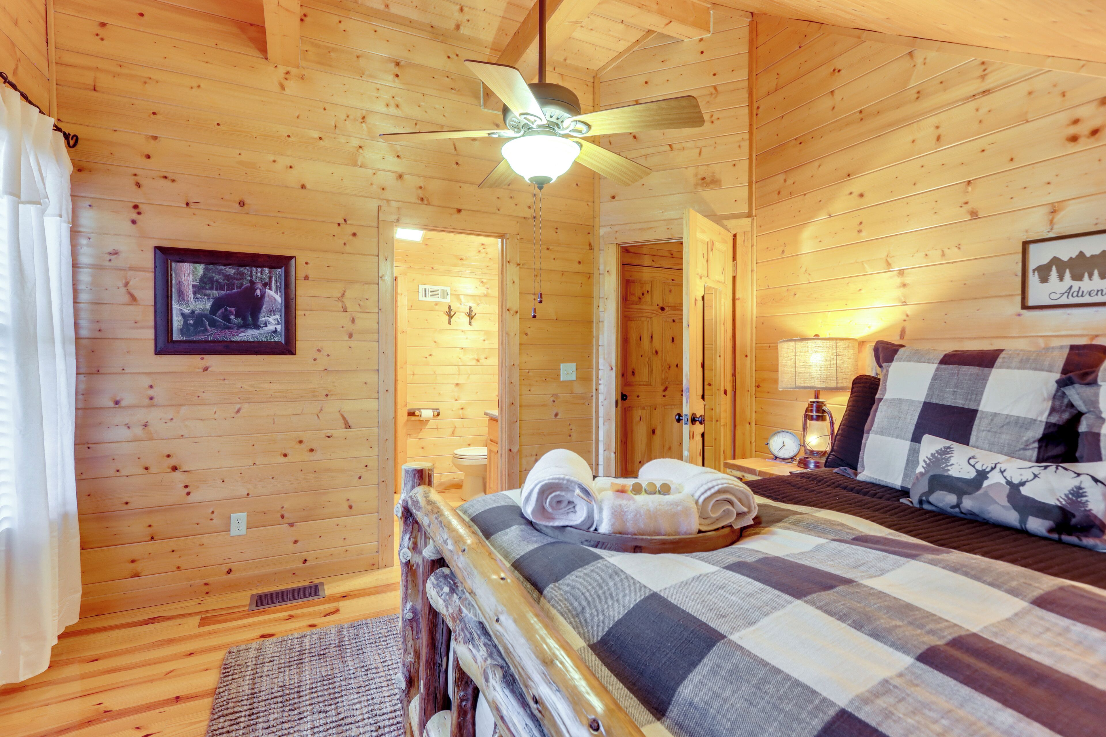 A wooden cabin bedroom with a bed, a ceiling fan, and a framed picture on the wall.