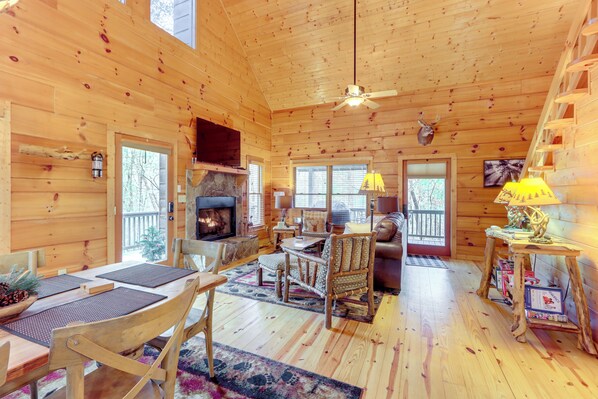A cozy cabin interior with a fireplace, wooden furniture, and a ceiling fan.