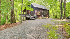 Un chalet rustique avec une allée en gravier, entouré de grands arbres.