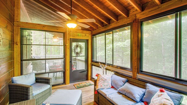Un intérieur de chalet chaleureux, avec des meubles en osier, de grandes fenêtres et un ventilateur de plafond.