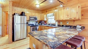 Une cuisine rustique, située dans une cabane en bois, avec un îlot en marbre, des appareils en acier inoxydable et des armoires en bois.