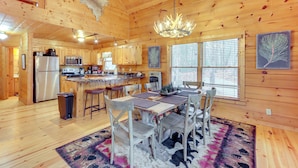 Une cabane en bois spacieuse, comprenant un coin repas, une cuisine et une grande fenêtre.