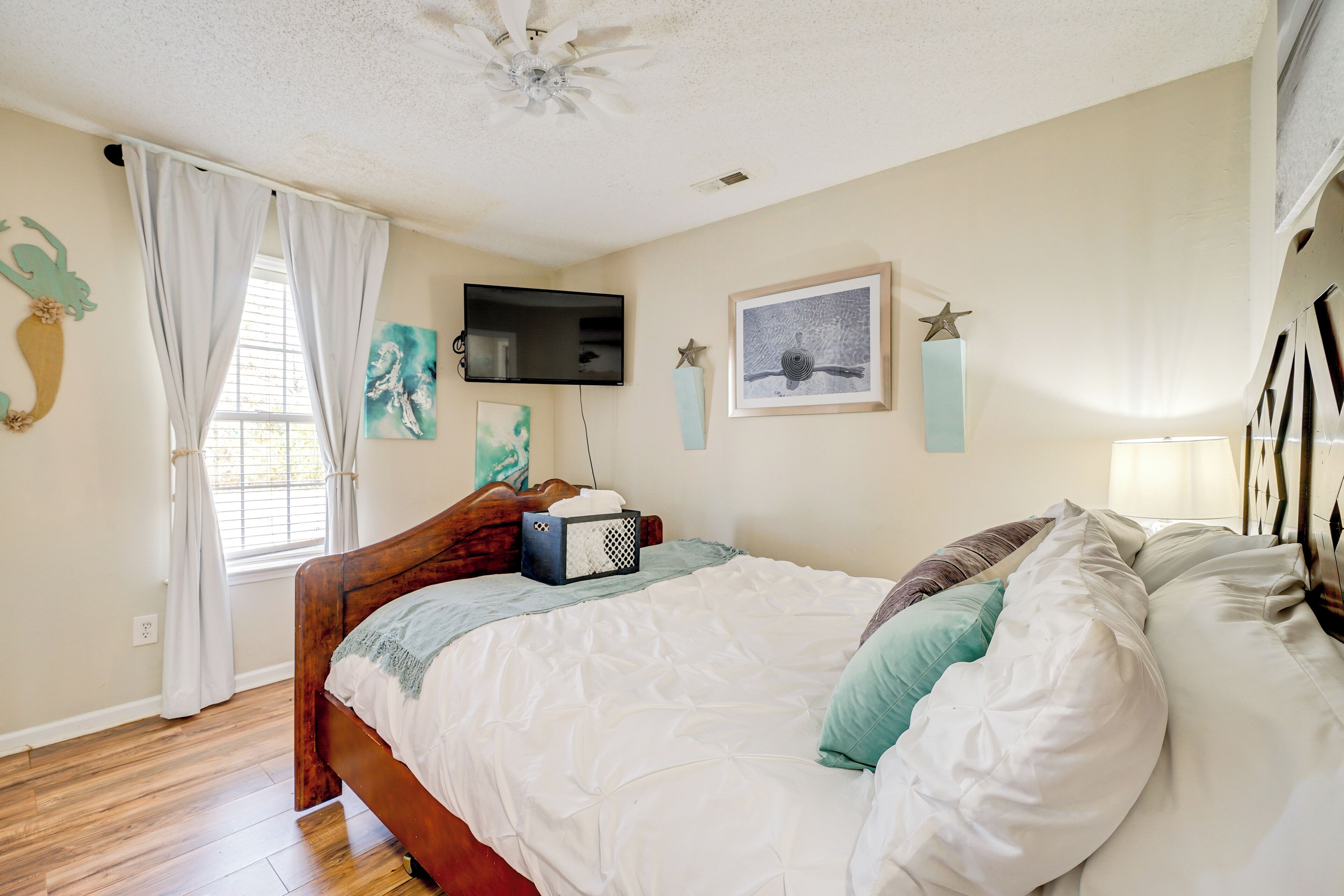 A bedroom with a wooden bed, white bedding, a mounted TV, and artwork on the walls.