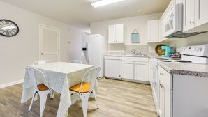 A compact kitchen with white cabinetry, a built-in microwave, and a dining area with a table and chairs. - 9 Mi to Shore: Family-friendly Sunset Beach Home (Sunset Beach)