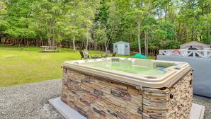 A hot tub with a stone exterior, surrounded by a grassy area and trees. - Community Pools & Hot Tub: Albrightsville Cottage! (Albrightsville)