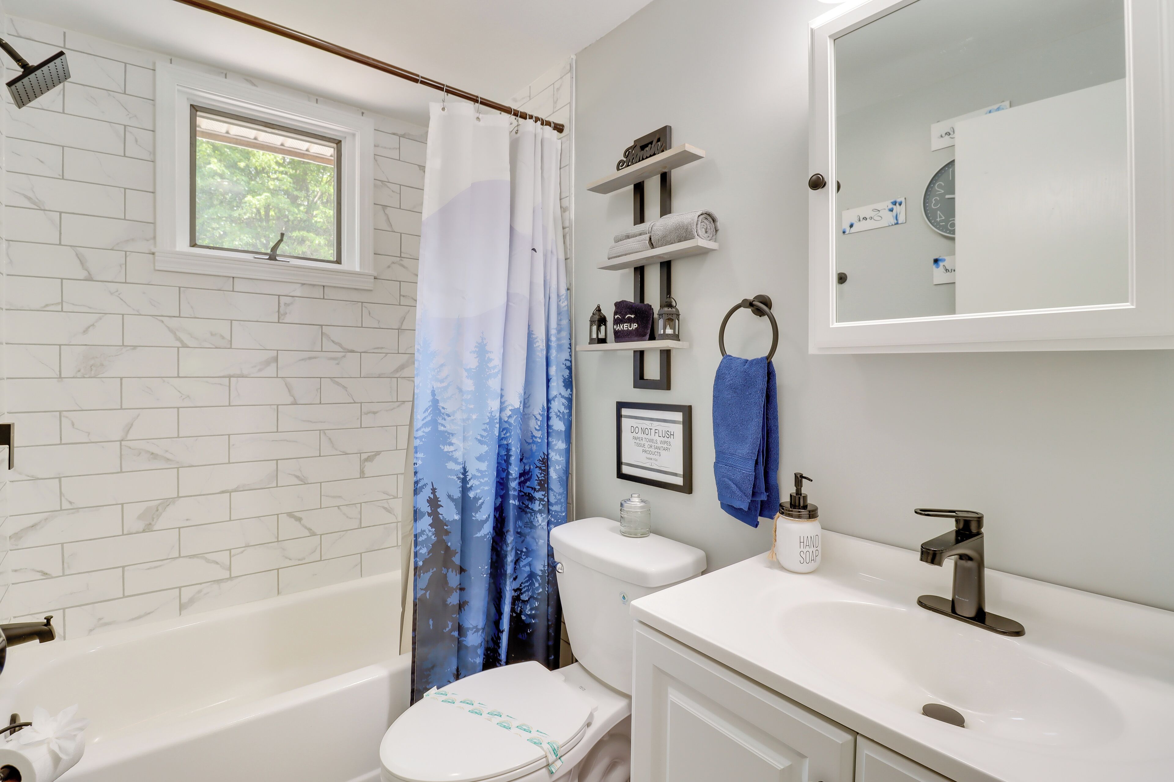 A bathroom with a bathtub, toilet, and sink. There is a window above the bathtub, a shower curtain, and a towel rack with towels.