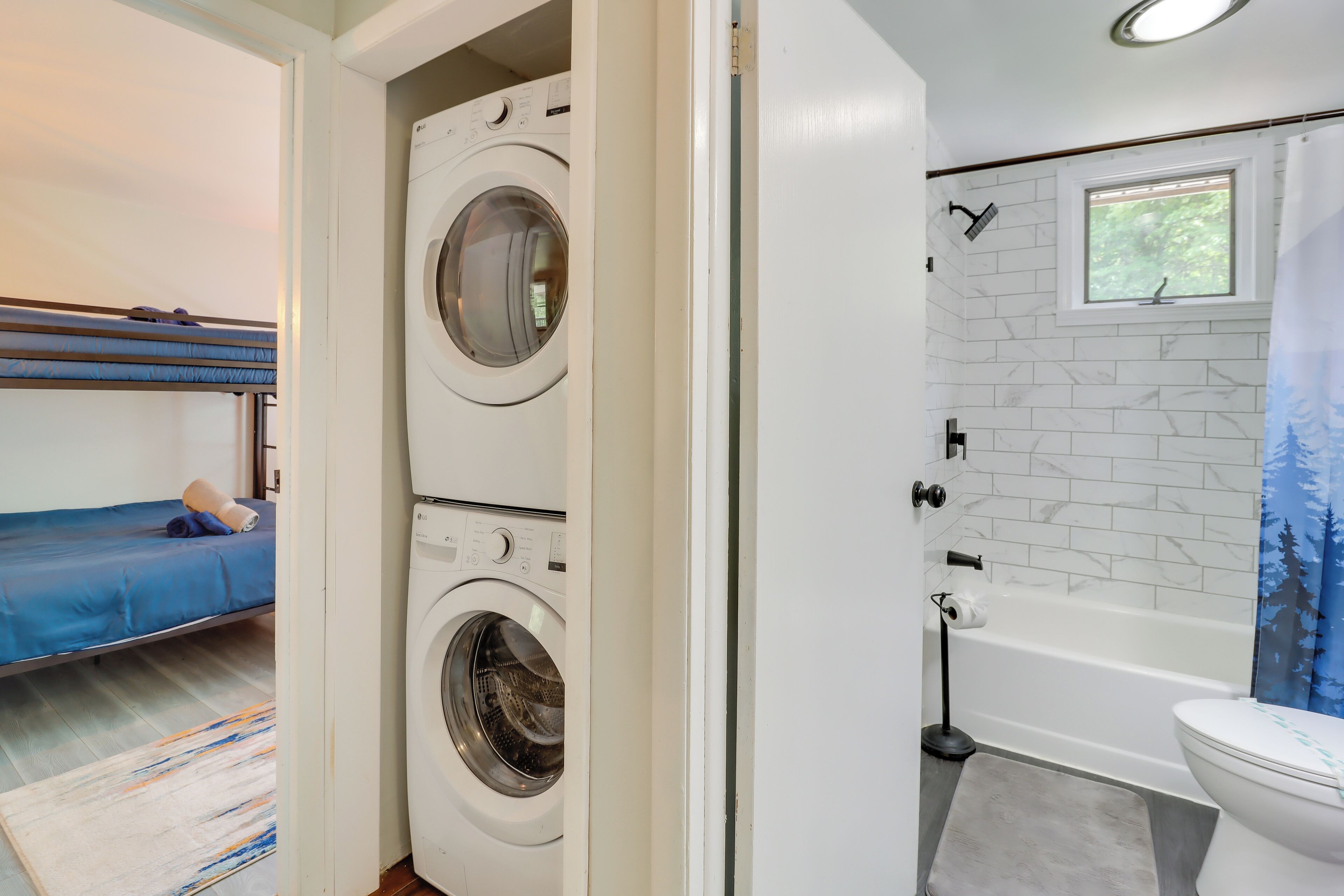 Une buanderie avec deux machines à laver, un lit avec un matelas bleu, une fenêtre et une salle de bain avec une baignoire et des toilettes.
