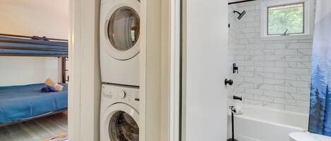 Une buanderie avec deux machines à laver, un lit avec un matelas bleu, une fenêtre et une salle de bain avec une baignoire et des toilettes.