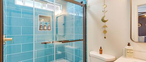 A bathroom with a glass shower enclosure, a toilet, and a sink with a mirror.