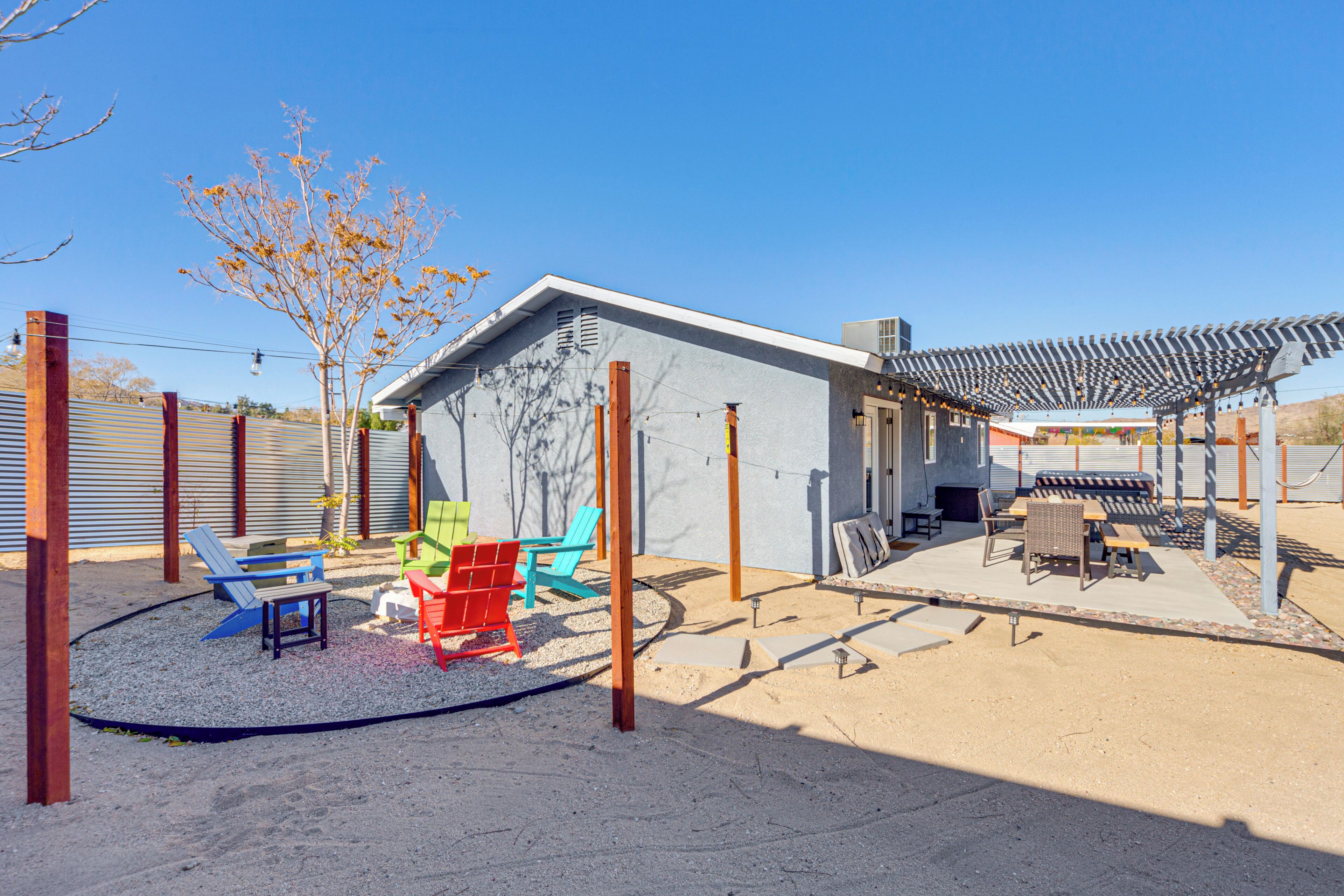 A modern outdoor patio area with a covered seating area, colorful chairs, and a small building with a sloped roof.