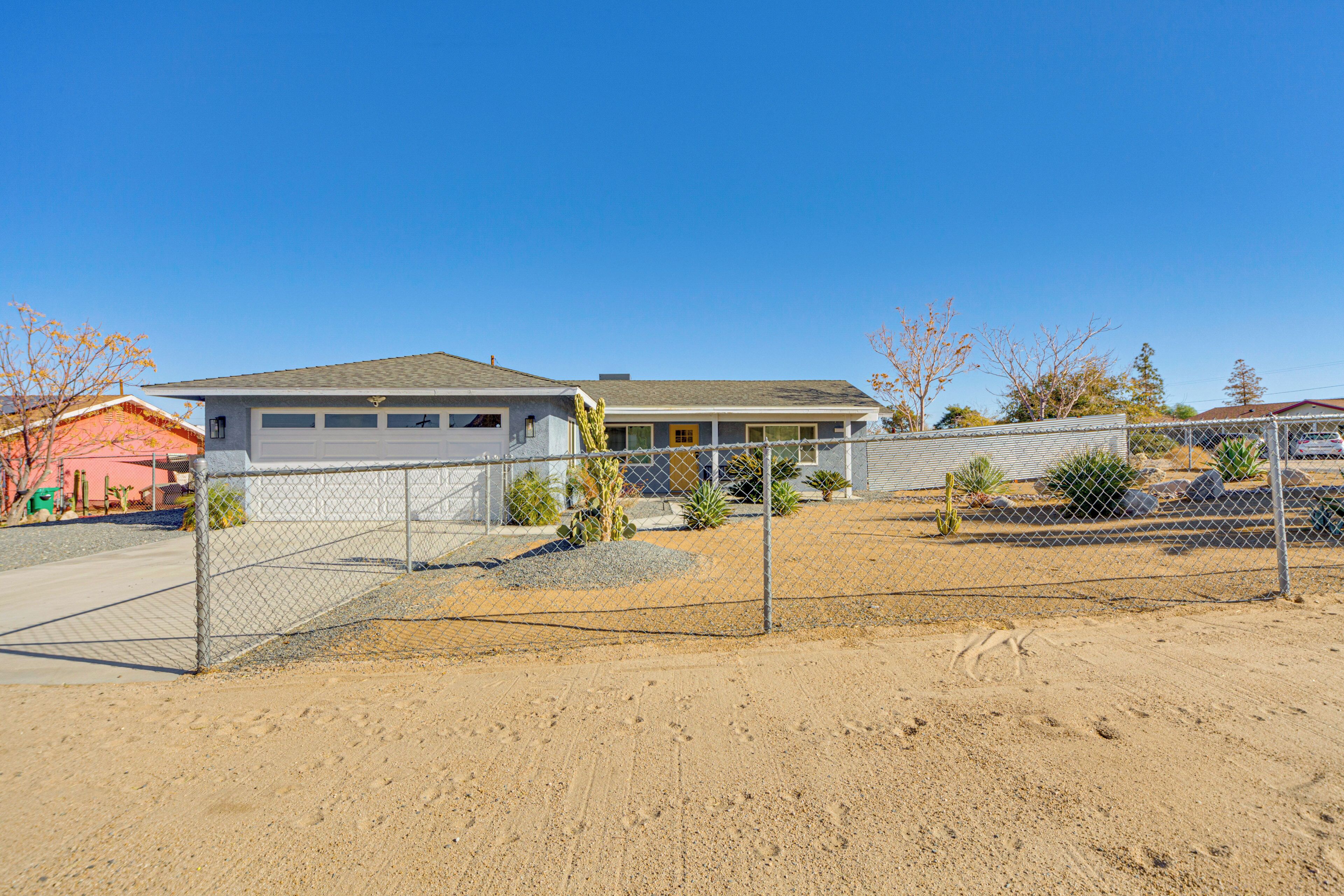 A residential house with a fenced yard, a garage, and a small garden with cacti and shrubs.