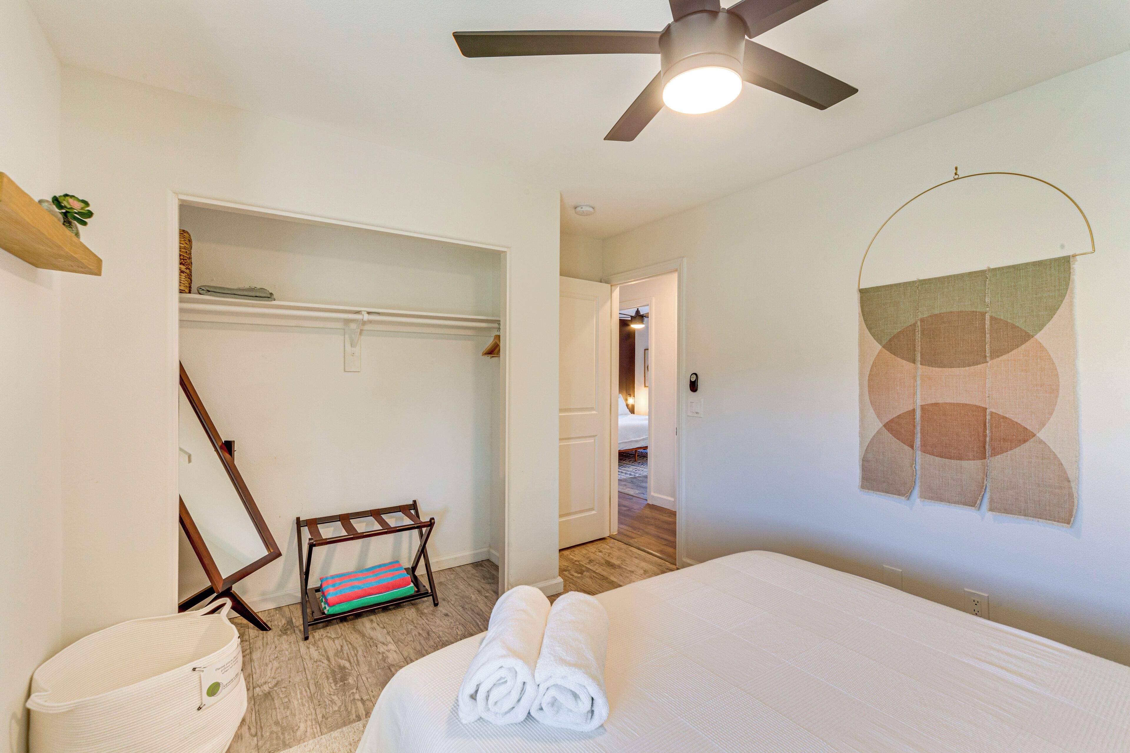 A hotel room with a bed, a ceiling fan, a wall-mounted towel rack, and a door leading to another room.
