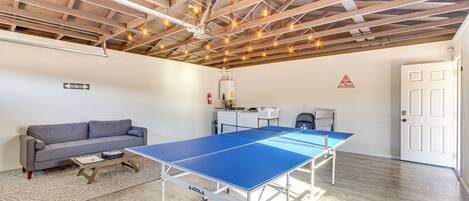 Una stanza con tavolo da ping pong, divano e scrivania con computer.