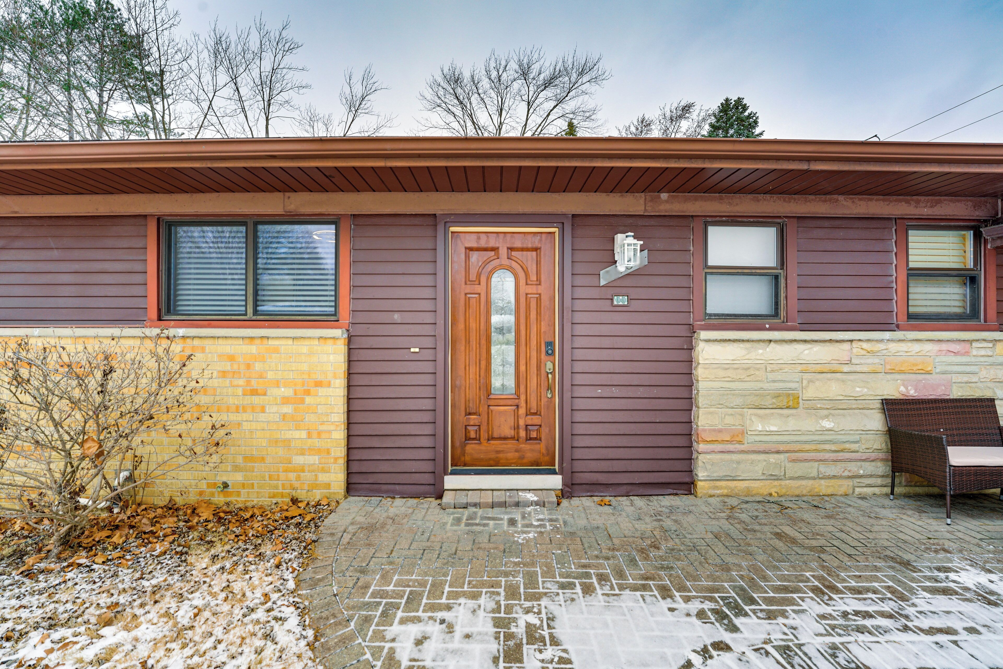 Une maison à deux étages avec un porche à l’avant, une porte en bois et un mur en briques.