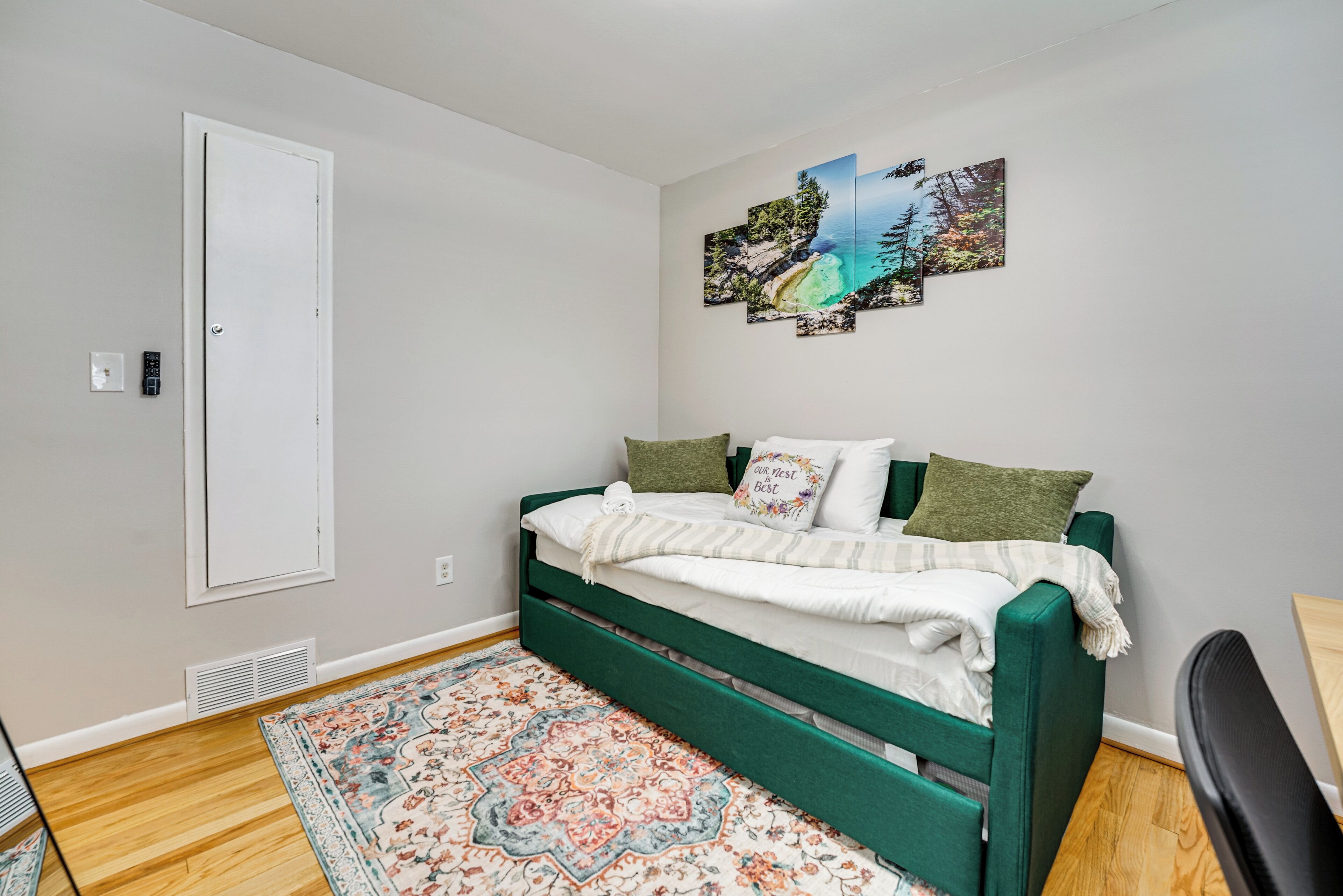 A bedroom with a green bed, a patterned rug, and a wall with three framed pictures.