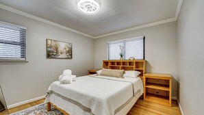 A bedroom with a large bed, wooden headboard, bedside tables, and a painting on the wall. - Fire Pit & Yard: Family Home in Farmington Hills! (Farmington Hills)