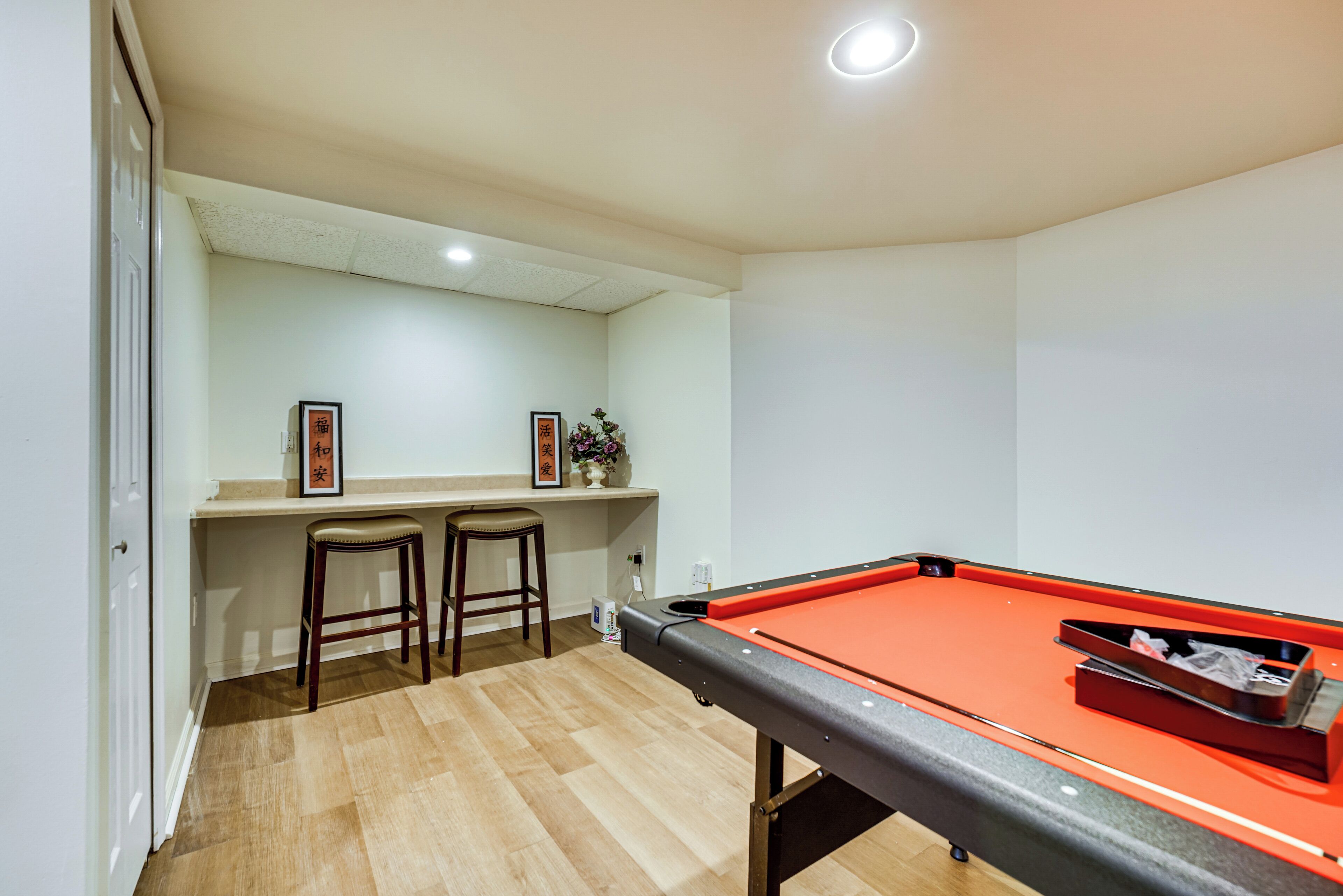 A pool table with two stools, a shelf with framed pictures, and a small plant.