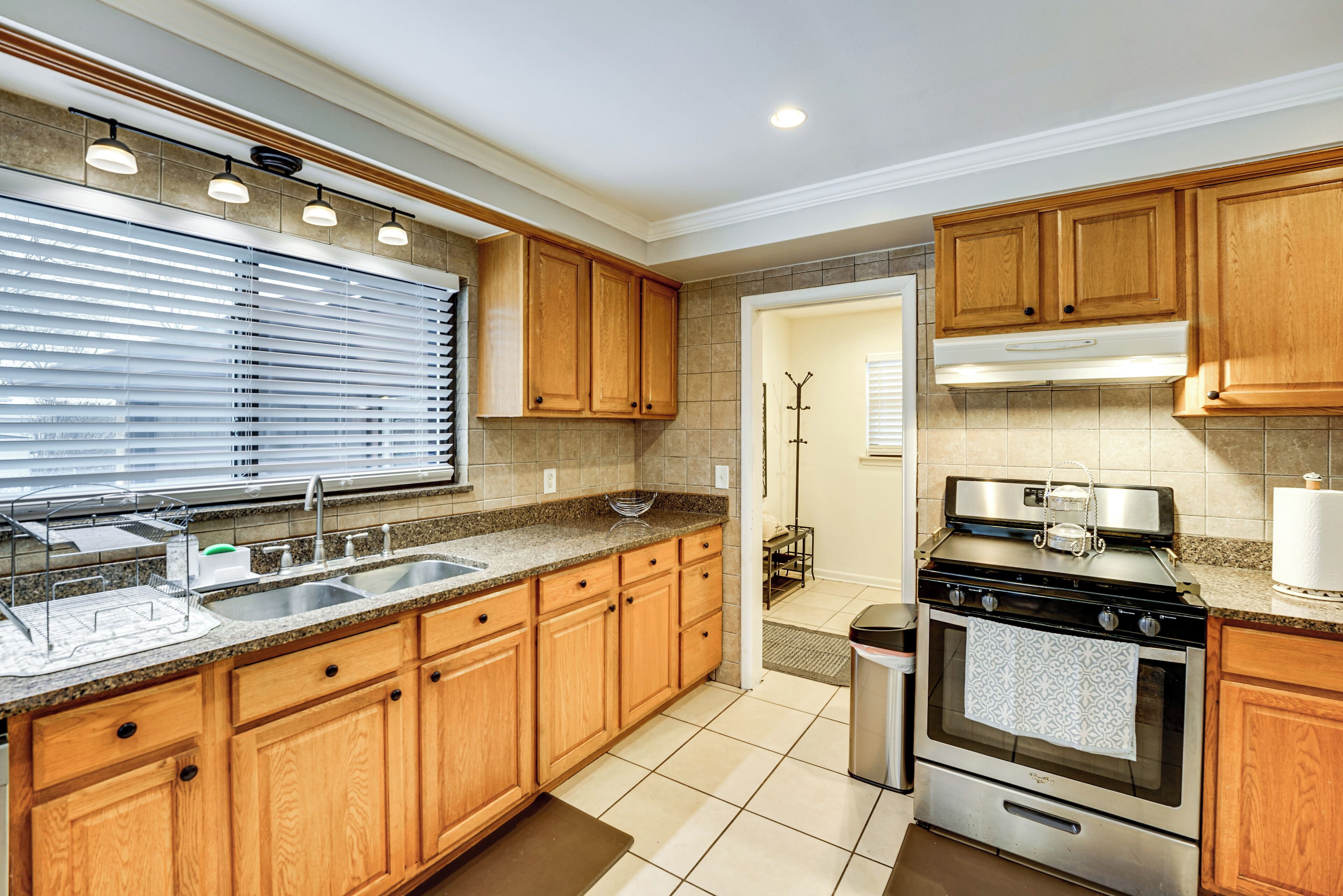 A modern kitchen with wooden cabinets, a stainless steel sink, a built-in oven, and a window with blinds.