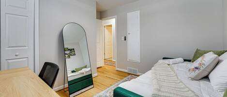 Un dormitorio con cama, escritorio, silla, espejo y puerta.