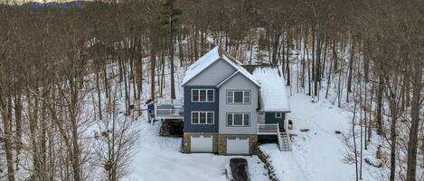 A two-story house with a snow-covered roof, surrounded by a forest.