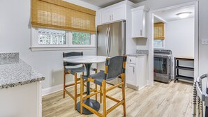 Eine moderne Küche mit weißen Schränken, einem Edelstahlkühlschrank, einem eingebauten Ofen und einem Essbereich mit rundem Tisch und zwei Stühlen.