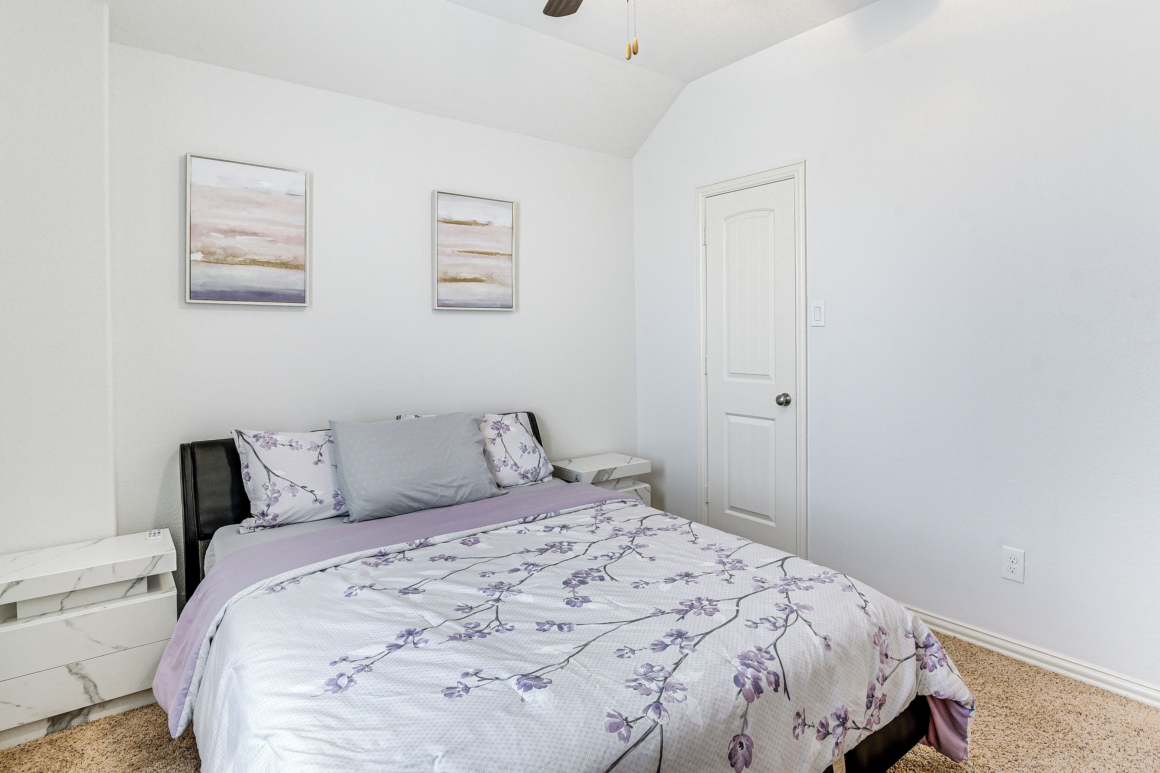 A bedroom with a bed, nightstands, a door, and two wall-mounted paintings.