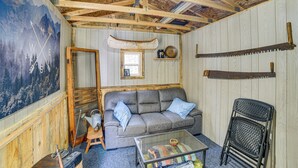 A rustic cabin interior with a wooden ceiling, a gray sofa, a glass coffee table, and a map mural on the wall. - Fish, Hike & Relax: Riverfront Manistique Cabin (Manistique)