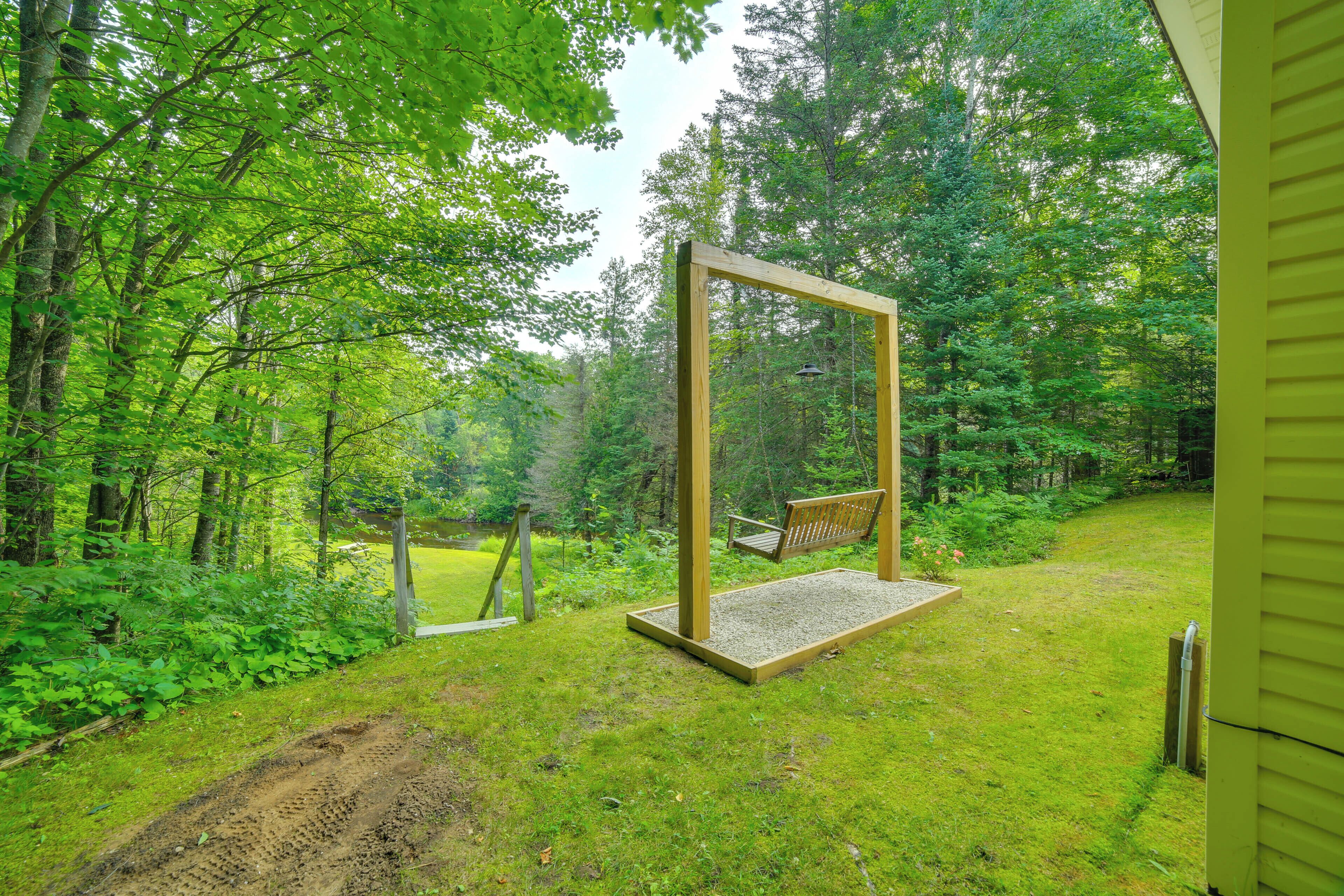 A wooden swing set in a lush green garden with a pond in the background.